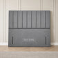 A gray upholstered headboard leaning against a cream paneled wall on a light wood floor