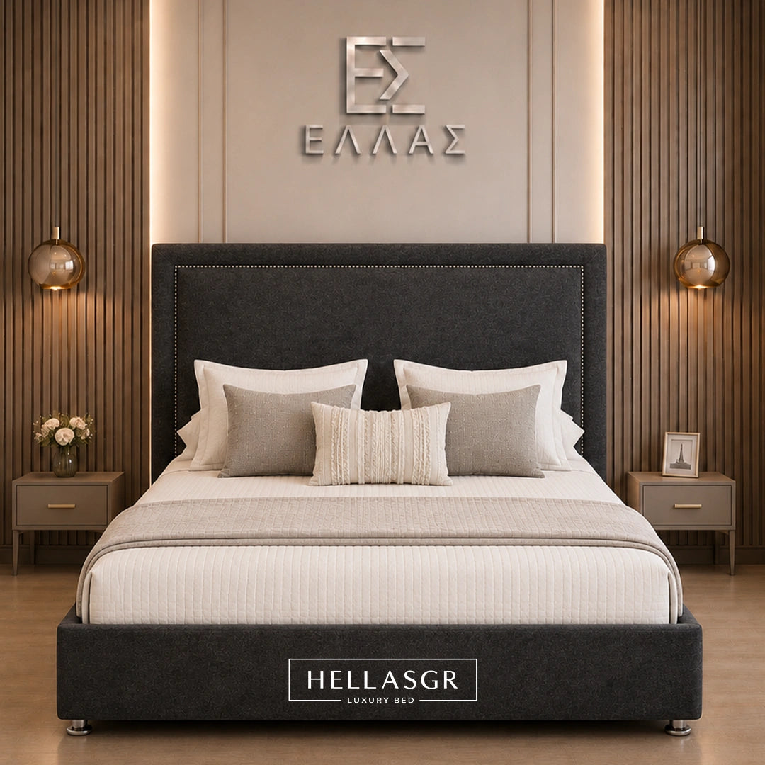A luxury upholstered bed centered in a modern bedroom setting. The bed frame is dark charcoal gray fabric with a tall matching headboard and a branded 'HELLASGR' plaque at the foot.