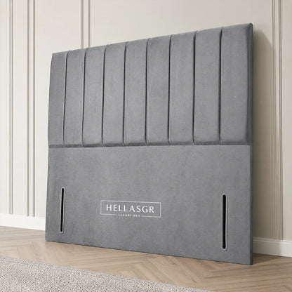 A gray upholstered headboard leaning against a cream paneled wall on a light wood floor
