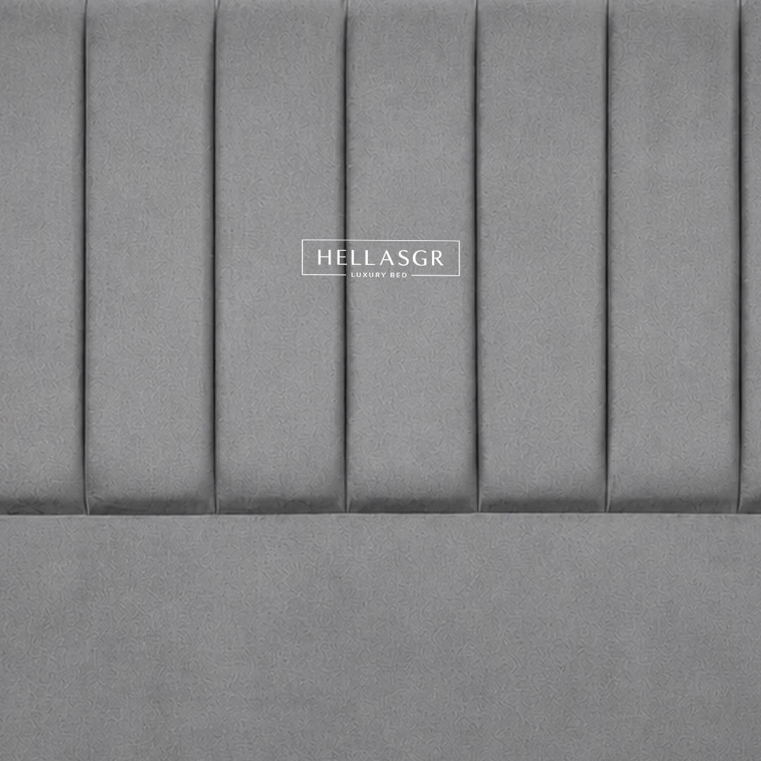 A gray upholstered headboard leaning against a cream paneled wall on a light wood floor