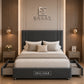 A dark gray upholstered bed frame with a tall padded headboard and matching footboard, styled in a modern bedroom. The bed is dressed in white and sage green bedding, with the brand name 'HELLASGR' visible on the footboard and wall.