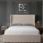 Beige upholstered Marina Elite bed with gray bedding against a dark paneled wall with a logo.